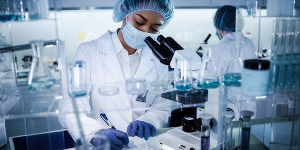 Scientist in protective gear working at microscope in laboratory
